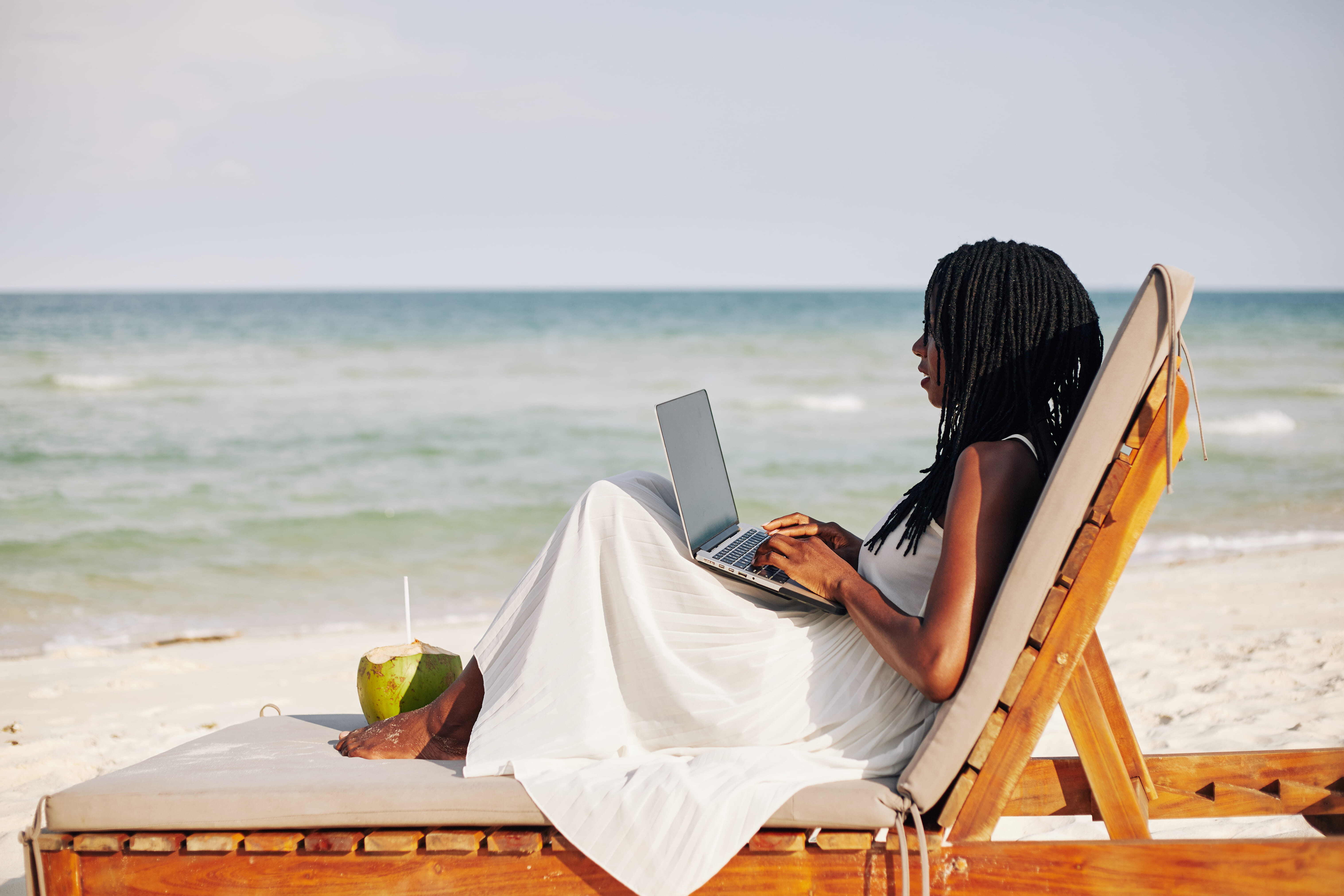 Young Travel Agent Woman Sitting at Beach Working on Laptop 